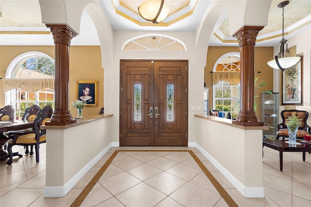 foyer featuring a tray ceiling, decorative columns, baseboards, and arched walkways