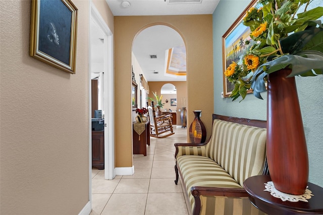 hallway with visible vents, baseboards, a textured wall, arched walkways, and light tile patterned flooring