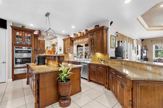 kitchen featuring brown cabinetry, a peninsula, decorative backsplash, appliances with stainless steel finishes, and a warming drawer