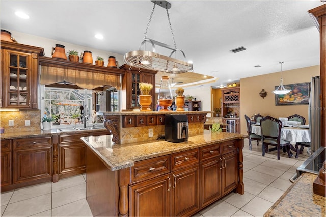 kitchen featuring visible vents, a kitchen island, light tile patterned floors, decorative backsplash, and hanging light fixtures