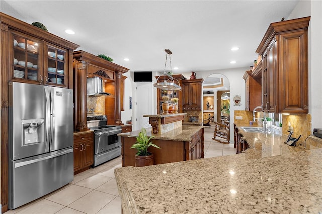 kitchen with a sink, light stone counters, stainless steel appliances, arched walkways, and decorative backsplash