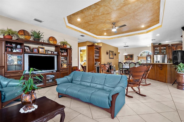 living area with a raised ceiling, light tile patterned floors, visible vents, and ceiling fan