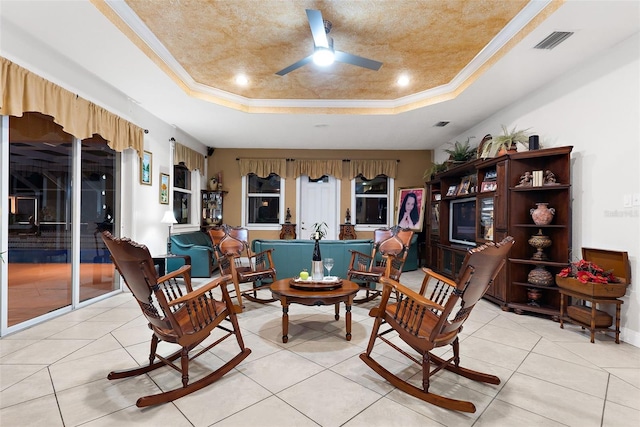 living area with visible vents, crown molding, a raised ceiling, and ceiling fan