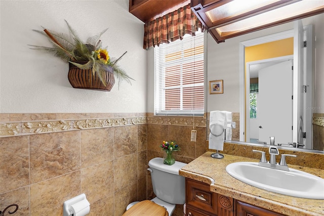 half bathroom with vanity, tile walls, toilet, and wainscoting