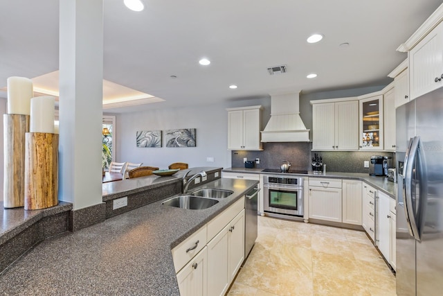 kitchen with backsplash, premium range hood, recessed lighting, appliances with stainless steel finishes, and a sink