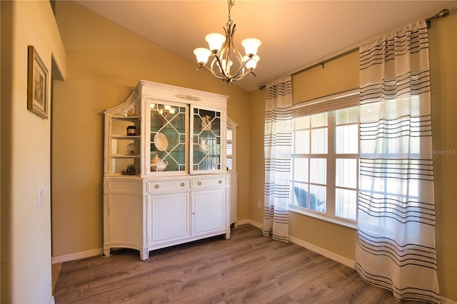 unfurnished dining area with lofted ceiling, wood finished floors, baseboards, and a chandelier