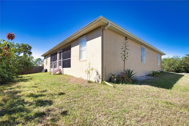 view of side of home with stucco siding, a yard, and fence