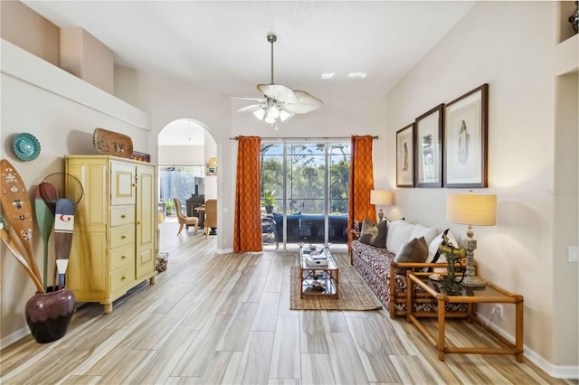 living room with arched walkways, baseboards, light wood-style floors, and a ceiling fan