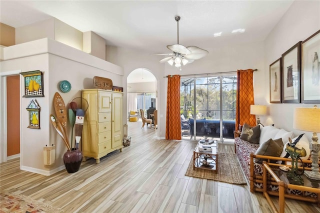 living room with light wood-type flooring, baseboards, arched walkways, and ceiling fan