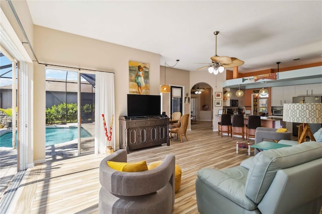 living area with light wood-style flooring, a ceiling fan, and arched walkways