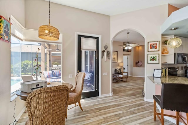 dining space with arched walkways, baseboards, light wood-type flooring, and ceiling fan