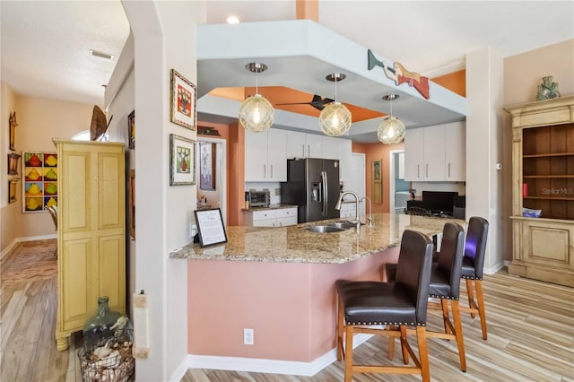 kitchen featuring visible vents, light wood finished floors, a peninsula, a sink, and refrigerator with ice dispenser