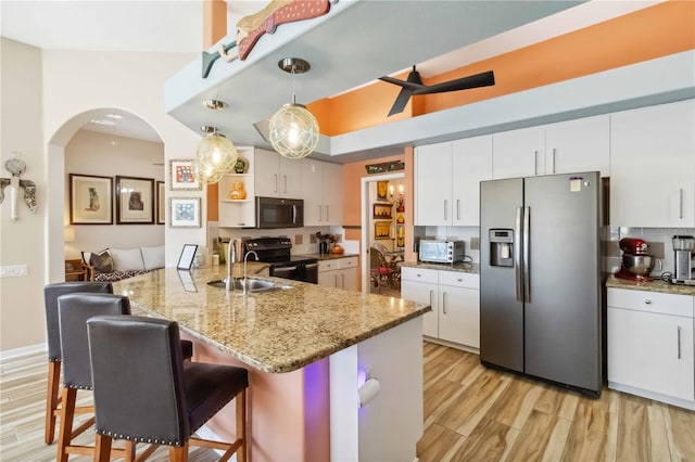 kitchen featuring light wood-type flooring, black range with electric stovetop, stainless steel fridge, arched walkways, and white cabinets