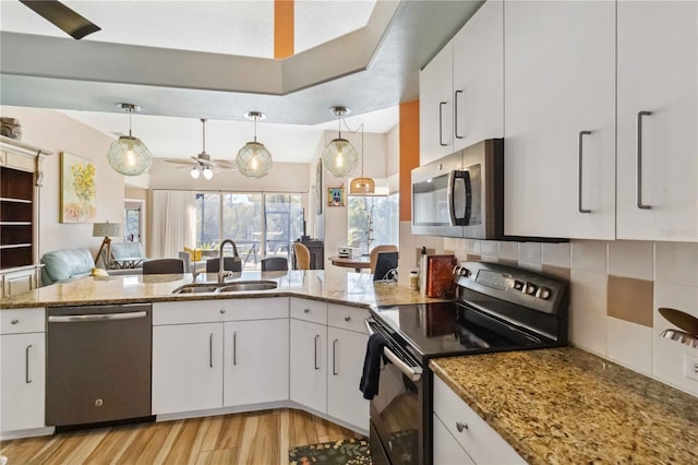 kitchen featuring light stone counters, a peninsula, a sink, decorative backsplash, and stainless steel appliances