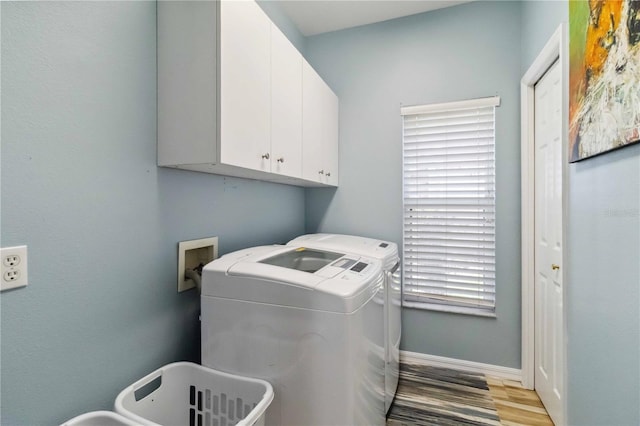 clothes washing area with washer and dryer, baseboards, cabinet space, and light wood-style floors