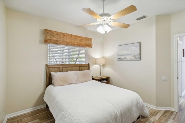 bedroom with ceiling fan, light wood-style floors, visible vents, and baseboards