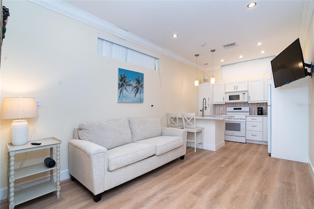 living area with recessed lighting, visible vents, light wood-style flooring, and crown molding