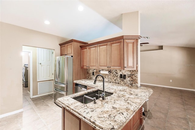 kitchen with a ceiling fan, light stone countertops, a sink, stainless steel appliances, and tasteful backsplash