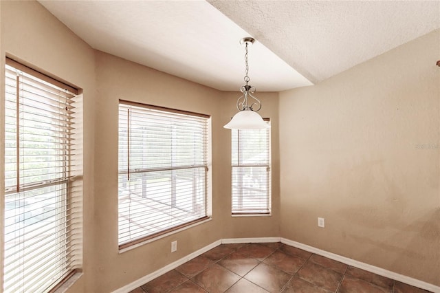 unfurnished dining area featuring dark tile patterned floors, baseboards, and a textured ceiling