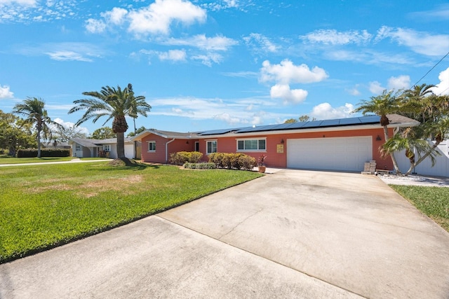 ranch-style house featuring a garage, roof mounted solar panels, concrete driveway, and a front lawn