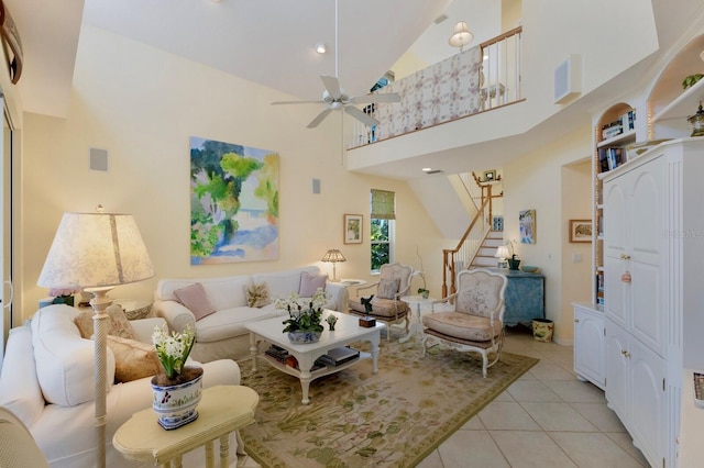 living room featuring light tile patterned floors, a ceiling fan, a towering ceiling, and stairs