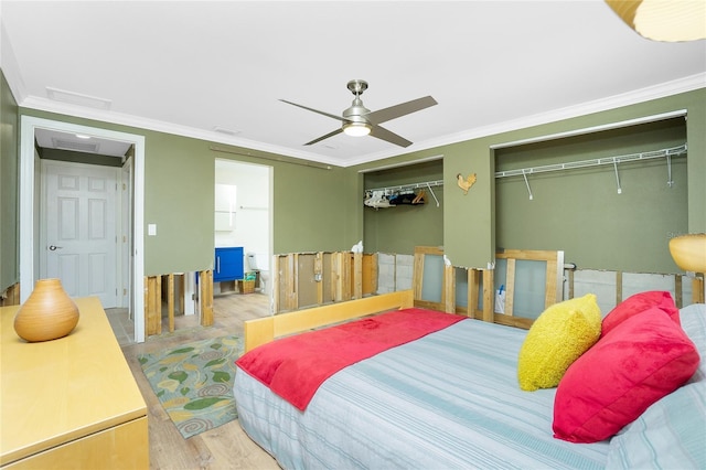 bedroom featuring two closets, wood finished floors, crown molding, attic access, and ceiling fan