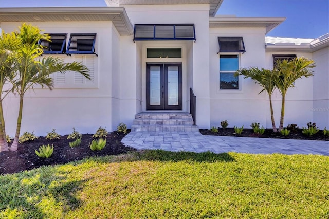 view of exterior entry with a lawn, stucco siding, and french doors