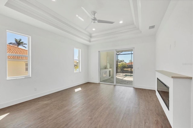 unfurnished living room with ornamental molding, baseboards, a raised ceiling, ceiling fan, and wood finished floors