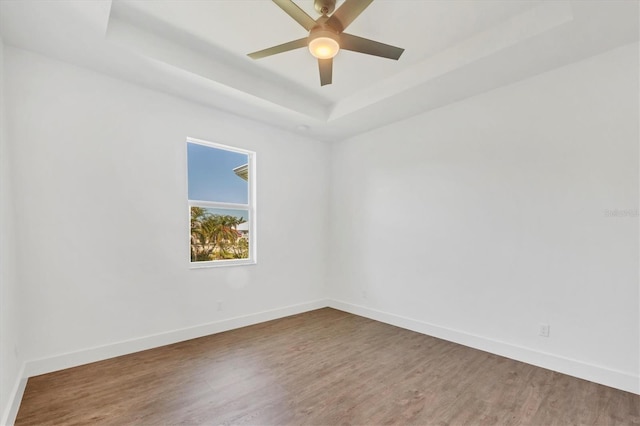 empty room featuring a tray ceiling, baseboards, wood finished floors, and ceiling fan