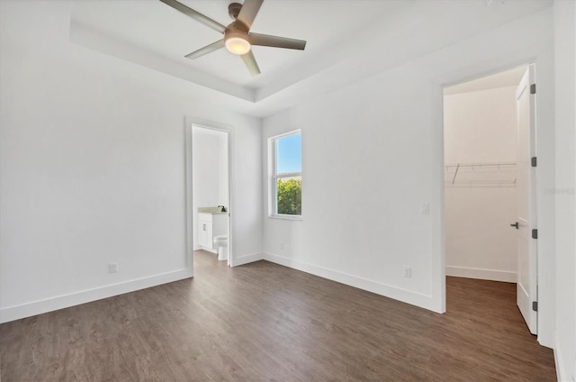 unfurnished bedroom featuring baseboards, dark wood-style flooring, a spacious closet, and a raised ceiling