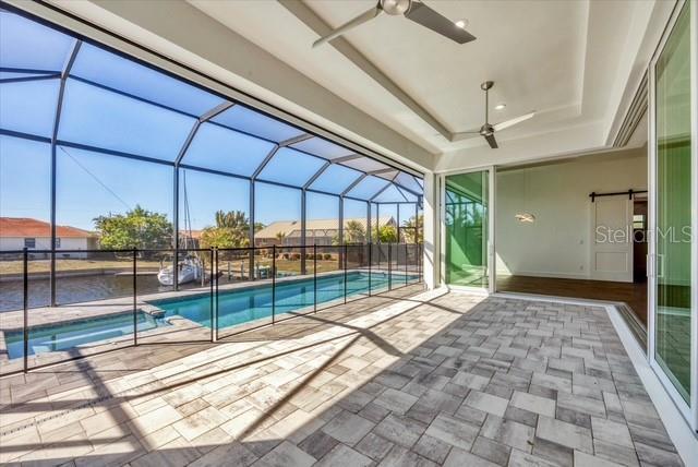 view of swimming pool with a pool with connected hot tub, glass enclosure, ceiling fan, and a patio area