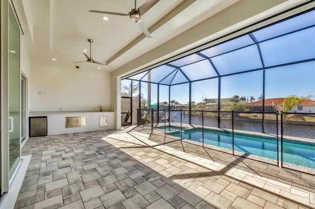 view of pool with glass enclosure, a water view, a patio, and a ceiling fan