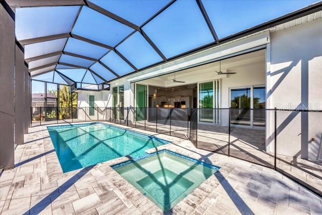 view of pool featuring a pool with connected hot tub, glass enclosure, ceiling fan, and a patio