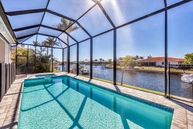 view of swimming pool featuring a pool with connected hot tub, a water view, glass enclosure, and a patio