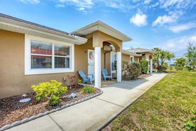 view of exterior entry featuring stucco siding and a lawn