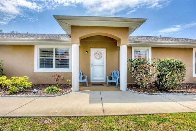 entrance to property with a shingled roof and stucco siding