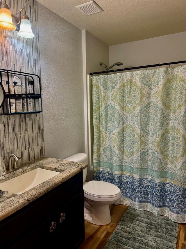 bathroom with toilet, vanity, wood finished floors, a textured ceiling, and visible vents