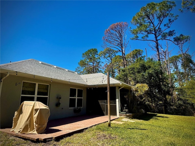 back of house featuring a shingled roof, a lawn, stucco siding, and a patio area