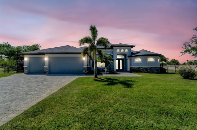 prairie-style house featuring a front yard, an attached garage, stucco siding, stone siding, and decorative driveway