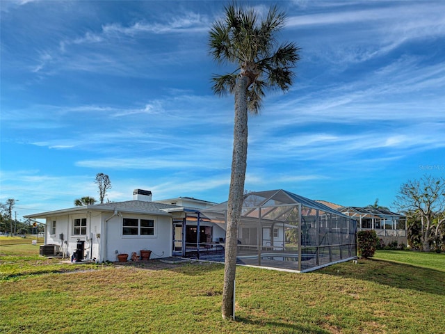 back of house featuring central AC unit, a chimney, a lawn, and a lanai