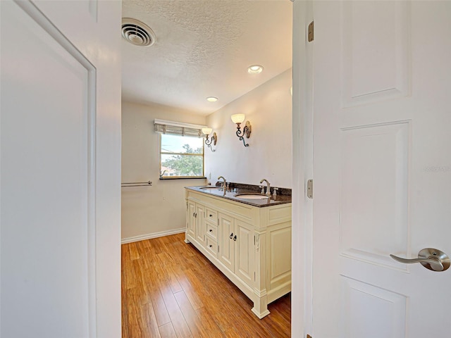 bathroom with visible vents, baseboards, a sink, a textured ceiling, and wood finished floors