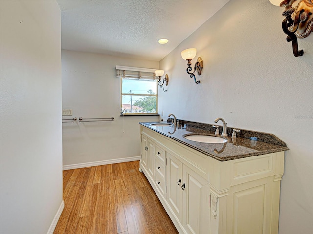 full bathroom with a textured ceiling, wood finished floors, a sink, and baseboards