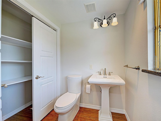 half bath featuring visible vents, baseboards, toilet, and wood finished floors