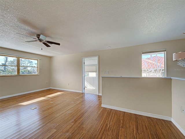 empty room featuring ceiling fan, baseboards, wood finished floors, and a healthy amount of sunlight