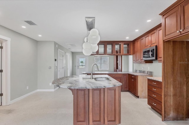 kitchen featuring light stone counters, a sink, brown cabinets, a breakfast bar area, and stainless steel microwave