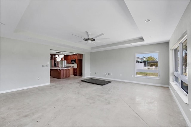 unfurnished living room with ceiling fan, baseboards, concrete flooring, and a raised ceiling