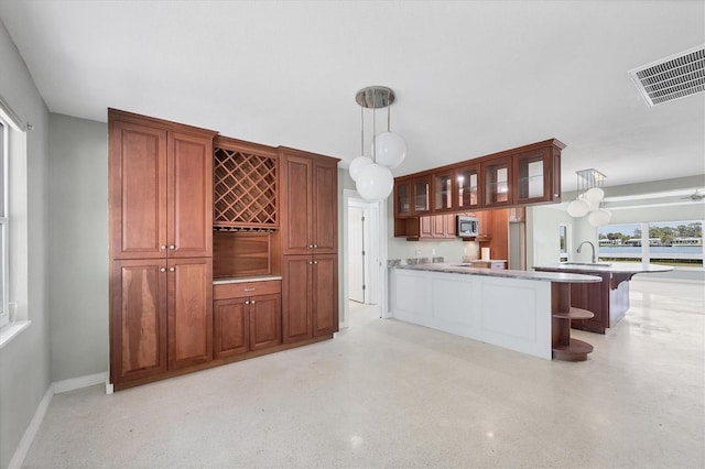 kitchen featuring visible vents, a sink, stainless steel microwave, a peninsula, and glass insert cabinets
