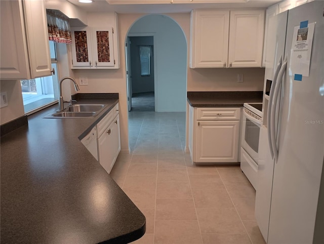 kitchen featuring arched walkways, white cabinetry, a sink, and white appliances
