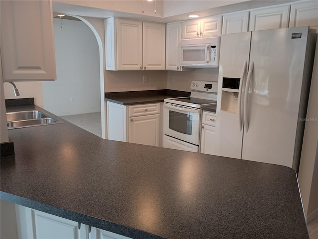 kitchen featuring dark countertops, a sink, arched walkways, white appliances, and white cabinetry