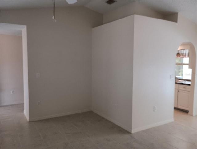 empty room featuring vaulted ceiling, visible vents, a ceiling fan, arched walkways, and baseboards